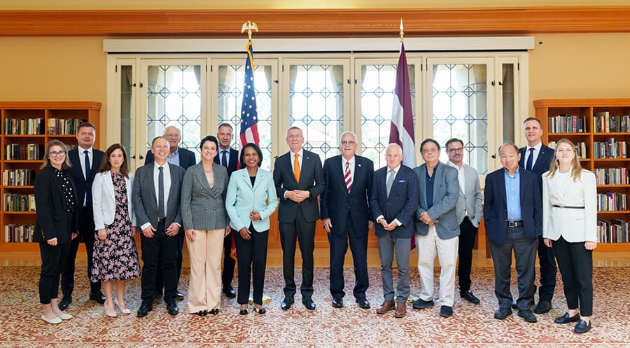 Group of people standing in front of a bank of windows in a library study room.