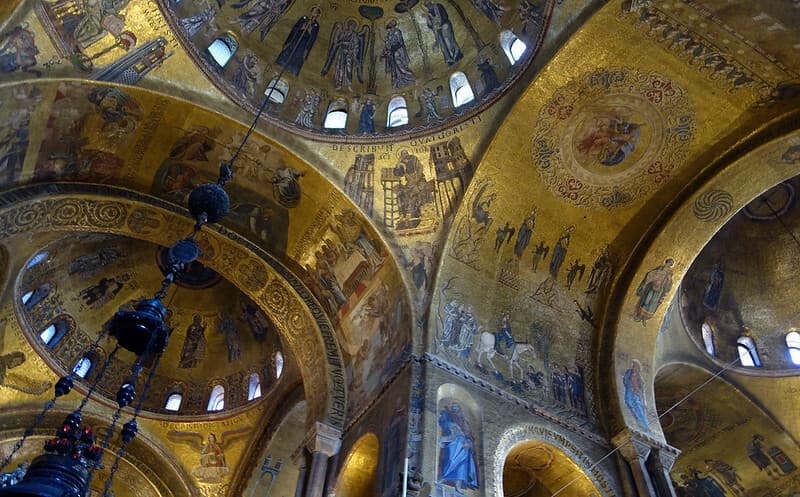 St Mark's Basilica showing golden-colored, ornate ceiling arches with scenic paintings.